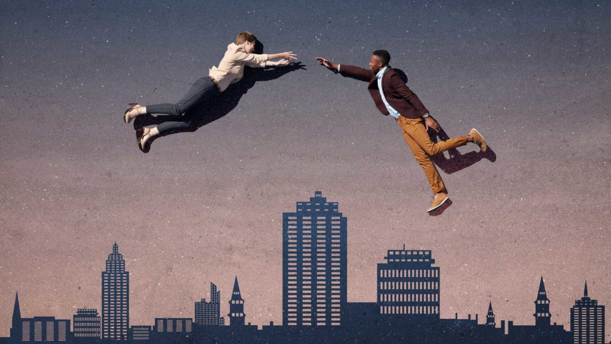 Two people in business attire jump high above a city as if to join hands and merge.