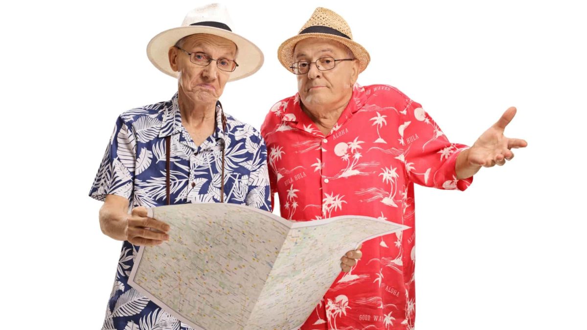 two older men wearing colourful tropical patterned shirts and hats like tourists puzzle over a map one is holding while he other holds up a hand as if indicating he doesn't know where they are going.