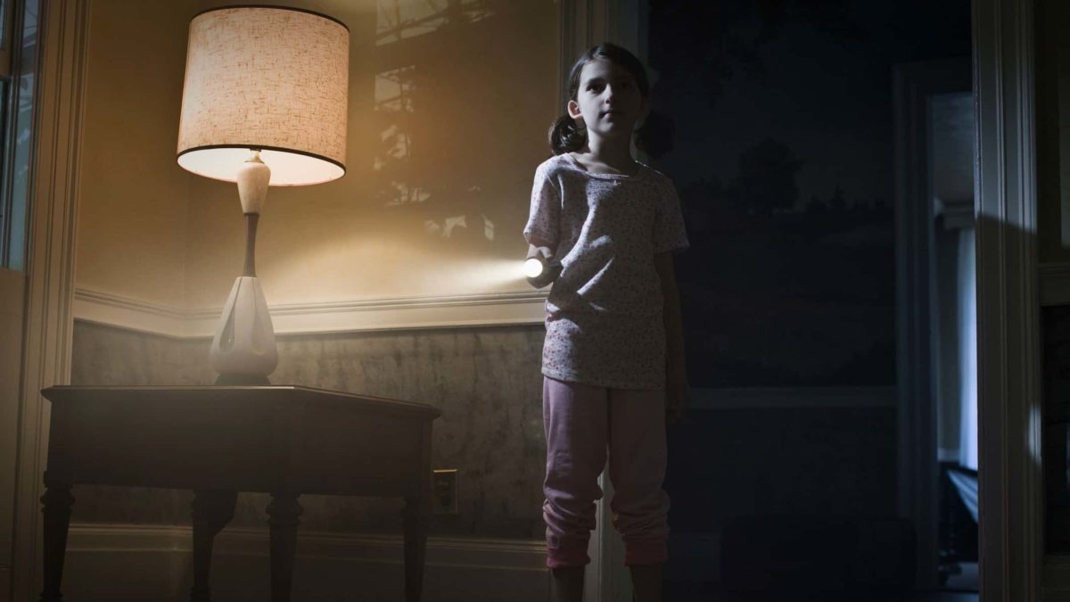 A young girl shines a flashlight in a dimly lit room of her house.