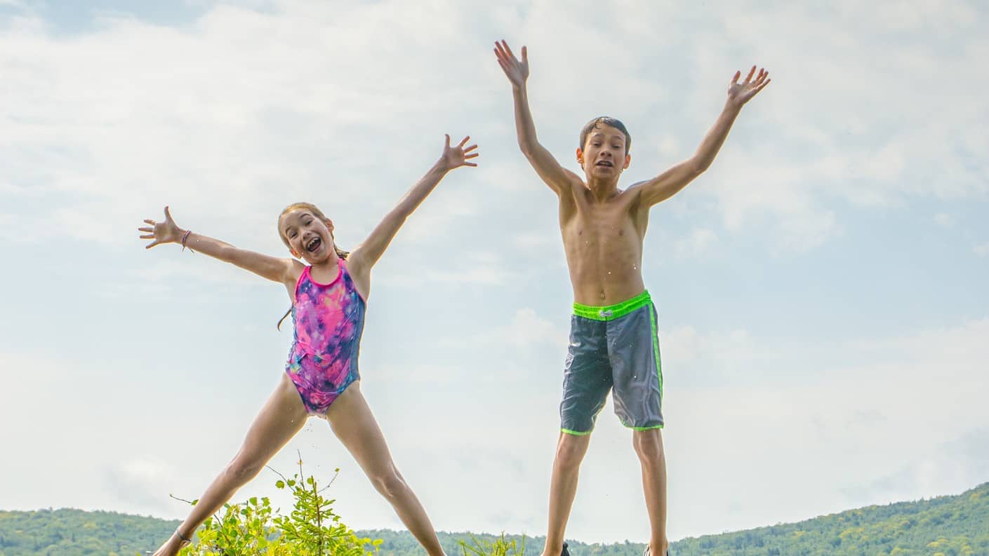 Two kids do big star jumps into the pool.