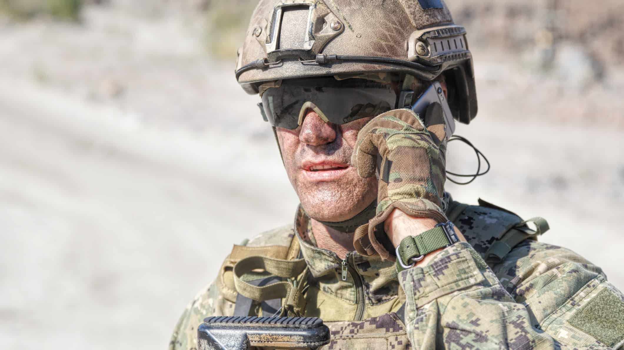 An Army soldier in combat uniform takes a phone call in the field.