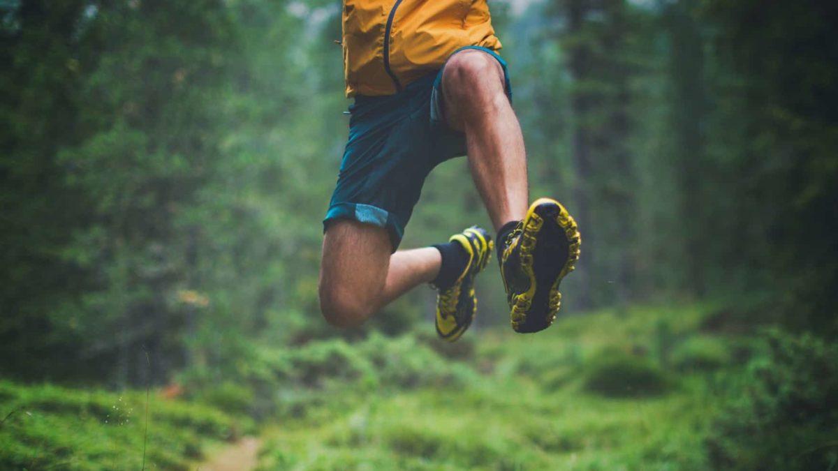 A person takes a huge leap as they run through a lush, green forest.