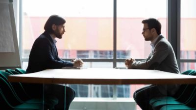 Two business people face off across the boardroom table.