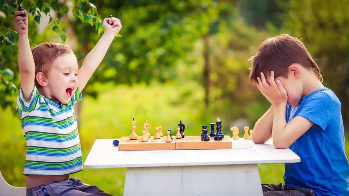 One boy is triumphant while the other holds his head in his hands after a game of chess.