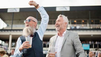 Two men dressed in their best cheer excitedly at a horse race, they've backed a winner.