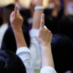 Two bidders raise their hands in the air to bid up the price of an ASX 200 share