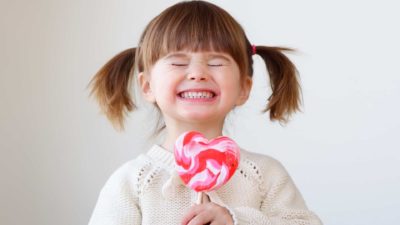 A little girl has a huge smile and a giant lollipop.