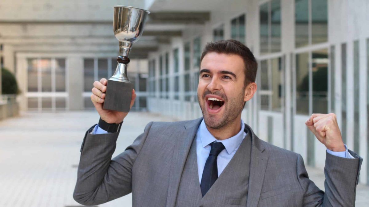 Businessman cheers while holding a trophy.