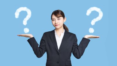 Woman in business suit holds both hands out with a question mark above each hand.