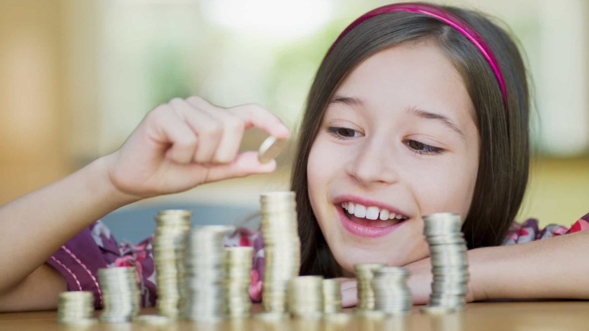 A young girl counts coins on a table.