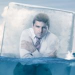 Man in business suit crouched and freezing in a block of ice.