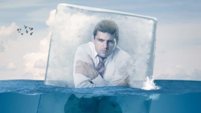 Man in business suit crouched and freezing in a block of ice.