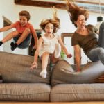 A woman and two children in the air over a sofa.