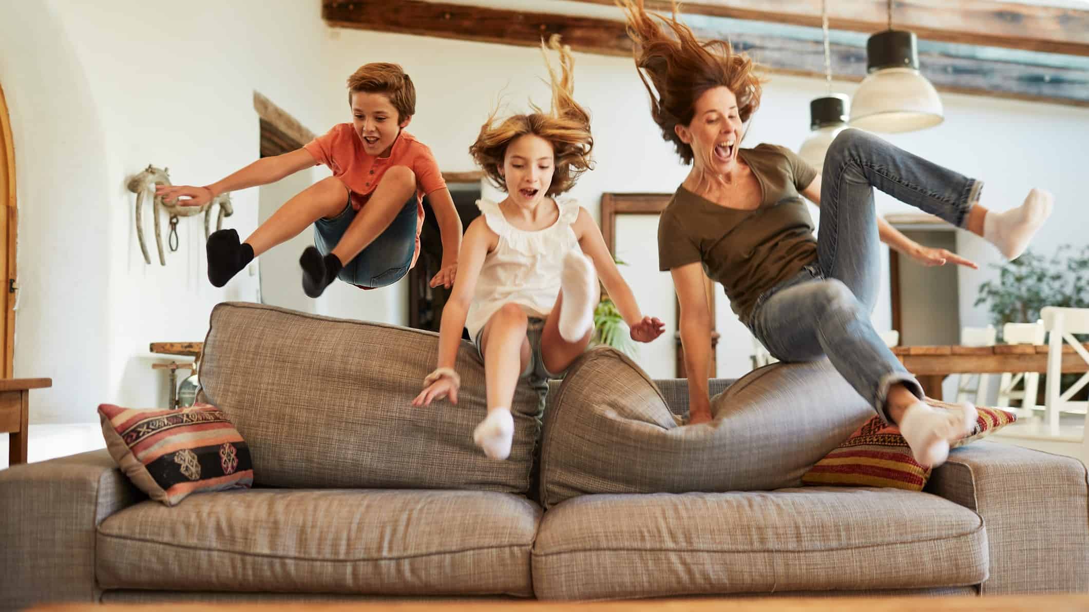 A woman and two children leap up and over a sofa.