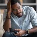 A disappointed man slumps in his chair and holds his head while playing an online game