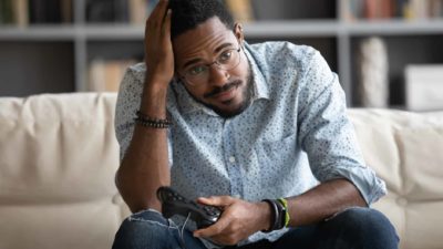 A disappointed man slumps in his chair and holds his head while playing an online game