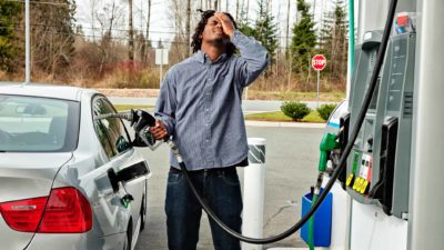 A man looks frustrated with hand on head as he fills up car at a service station.