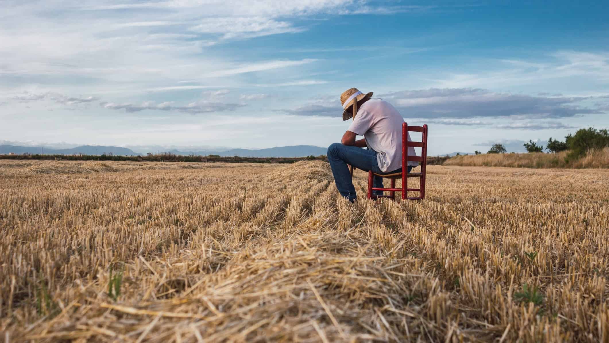Man sits on a chair in field of grain with head in hands.