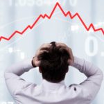 Man stands with head on his hands in front of a downward graph.