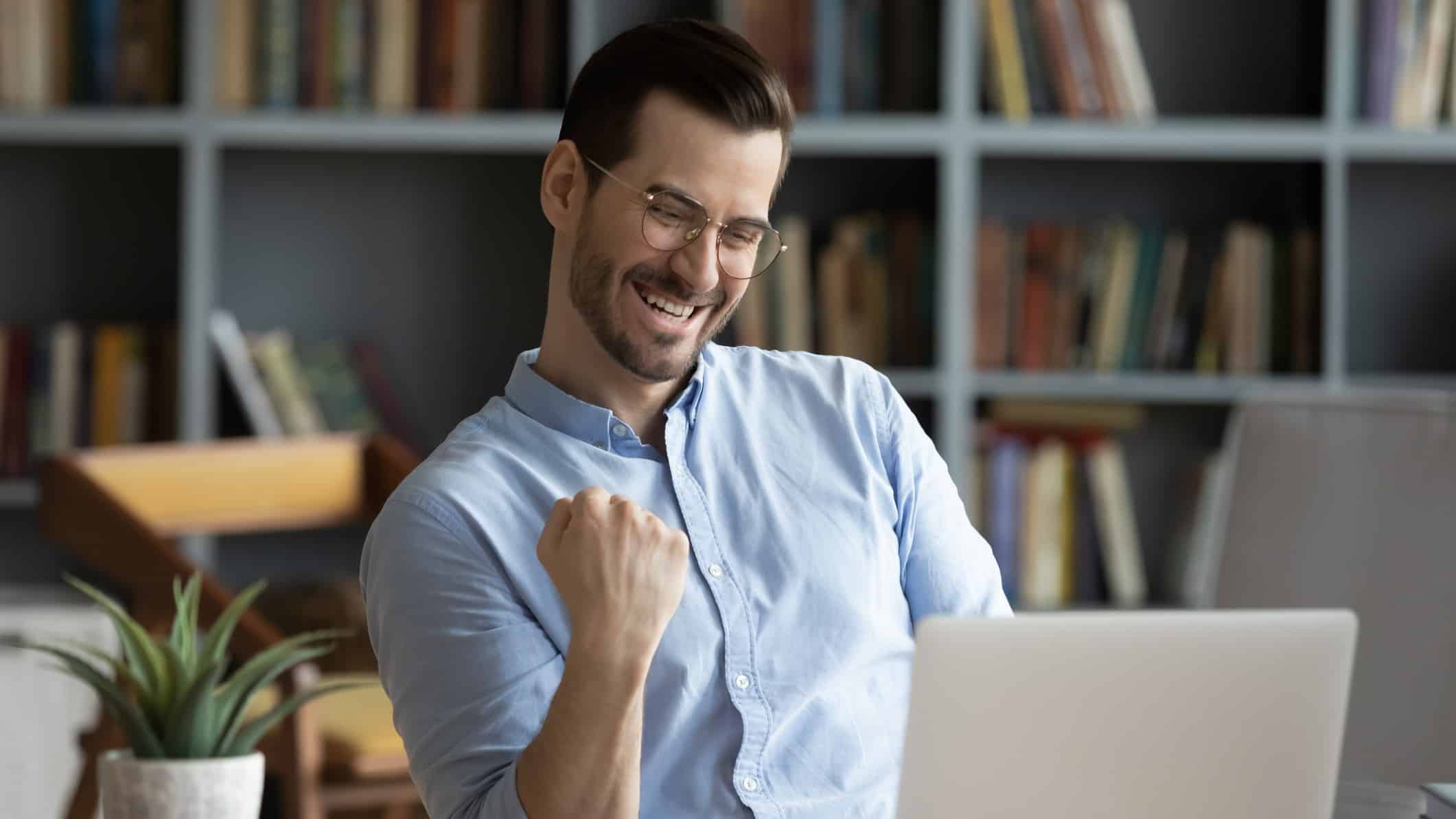 A man in a blue collared shirt sits at his desk doing a single fist pump as he watches his Neometals shares rising on his laptop