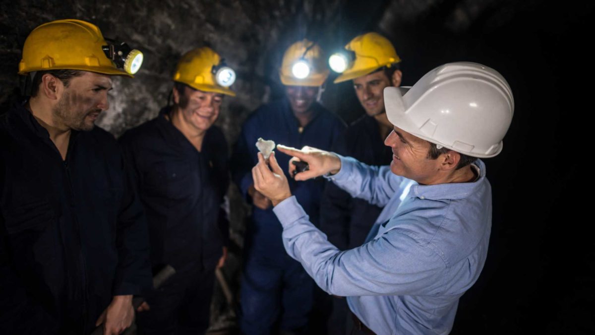 A miner holds up a mineral find as other workers look on,