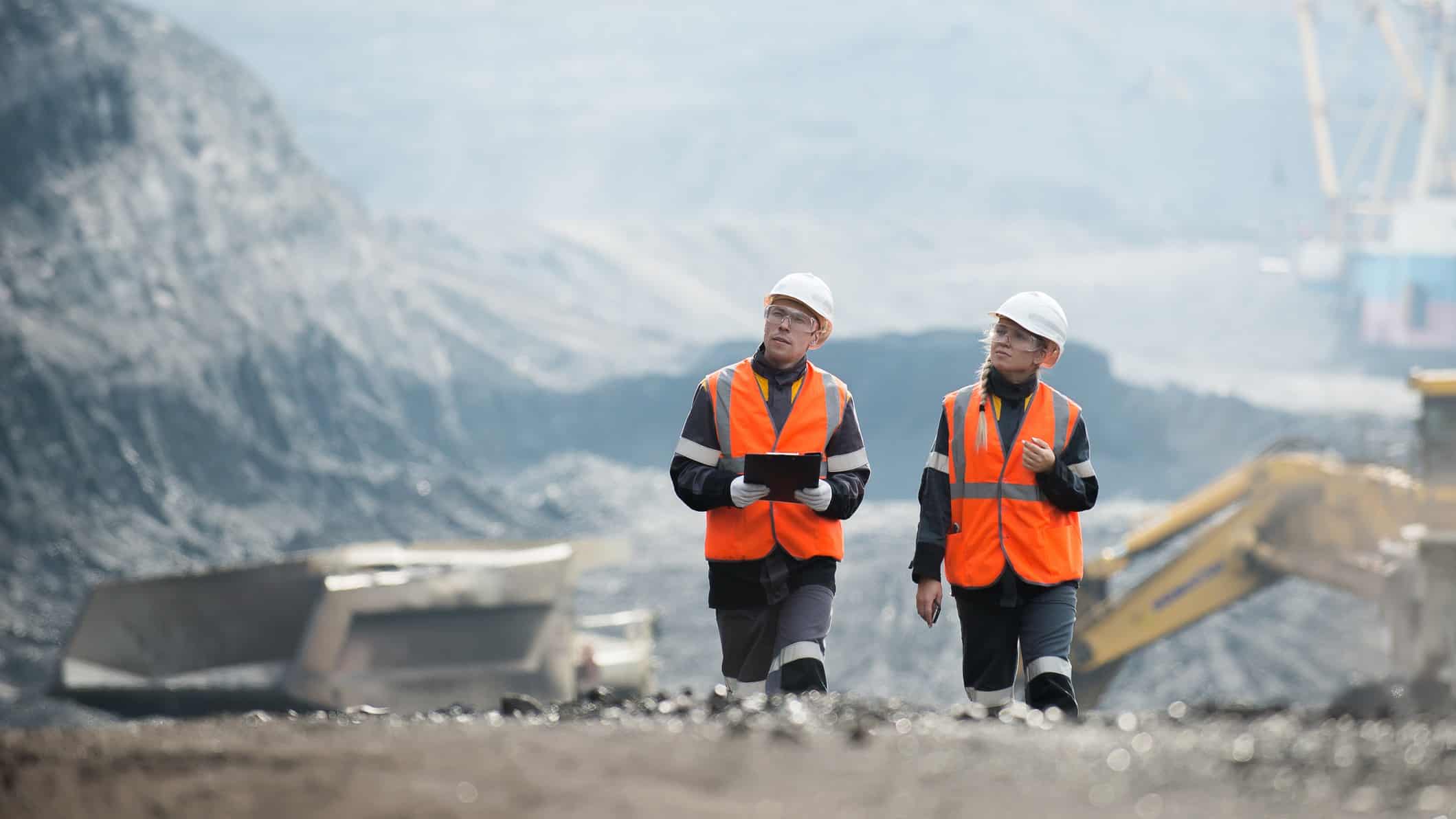 Two mining workers in orange high vis vests walk and talk at a mining site