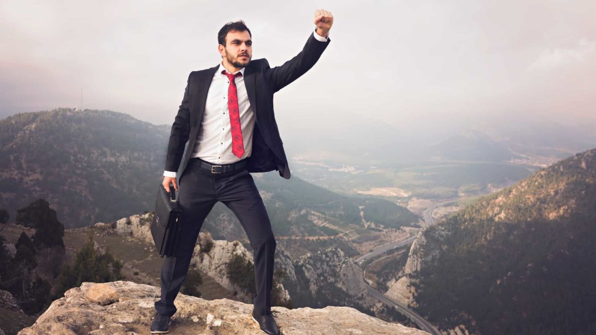 Young businessman standing on the top of the mountain punching fist in the air.