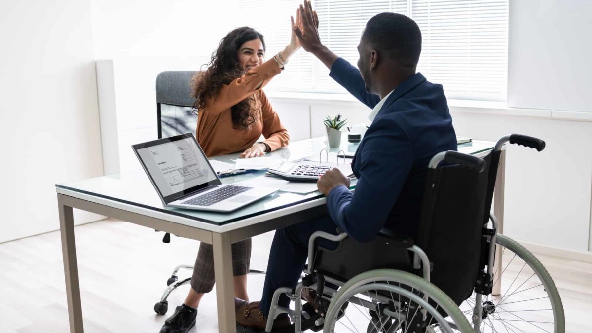 A woman and a man in a wheelchair celebrate new business with a high five across the desk.