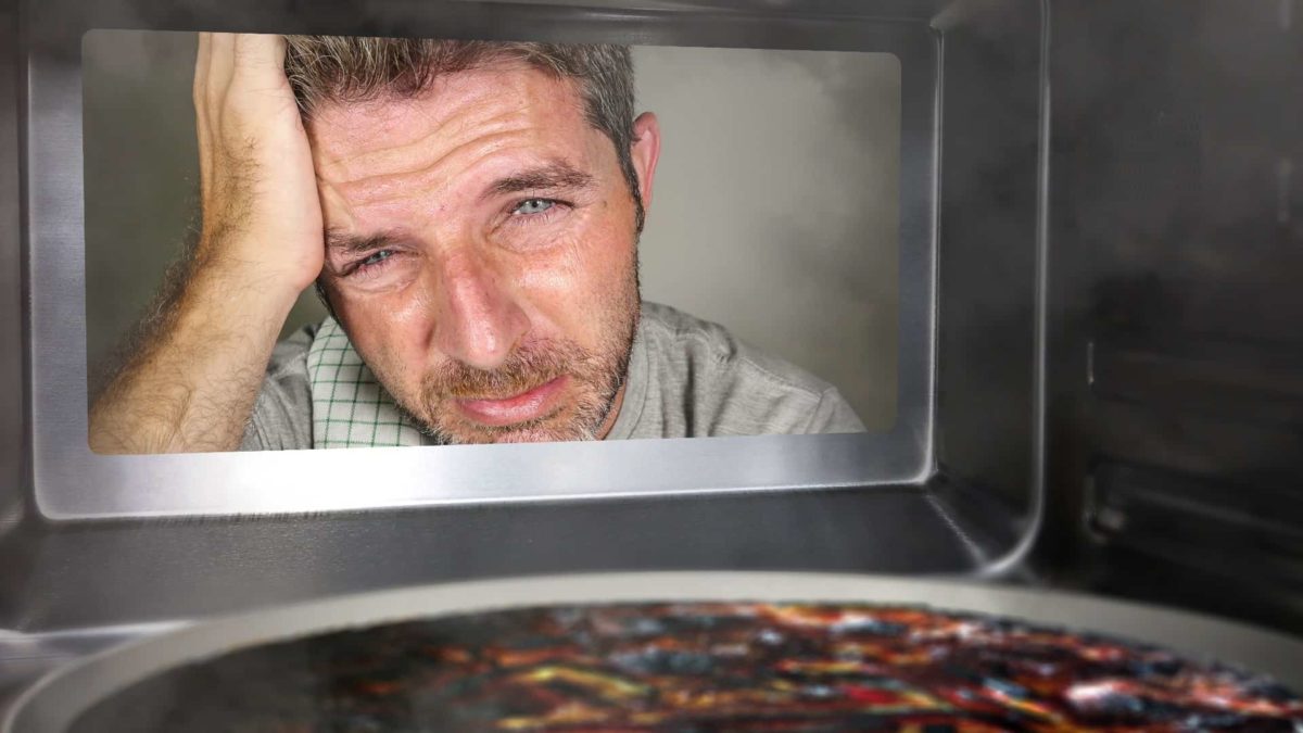 Unhappy man looks into oven at burnt pizza.