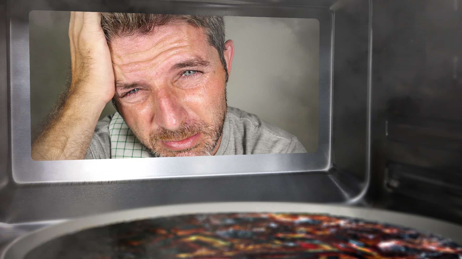 Unhappy man looks into oven at burnt pizza.