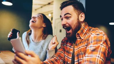 Excited male and female hipsters rejoice in good news received on their mobile phones.