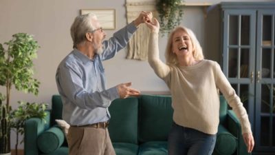 An older couple dance in their living room as they enjoy their retirement funded by ASX dividends