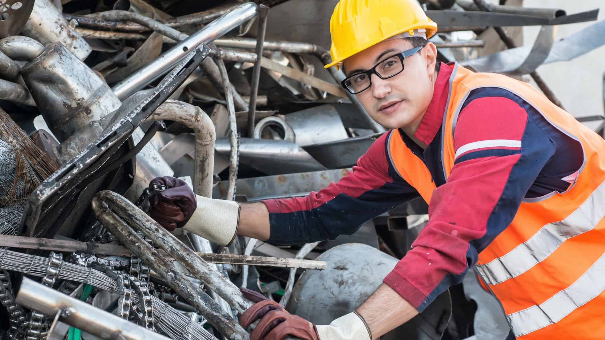 Worker in hard hat in front of pile of scrap metal.
