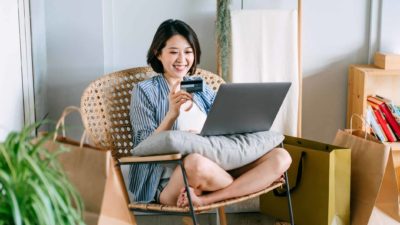 A woman sits on a chair smiling as she shops online.