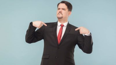 A smug Bendigo Bank investment manager in a suit and tie points to himself with both hands feeling proud that the Bendigo Bank share price is one of the best performing stocks in 2022