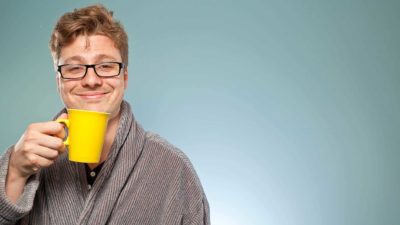 An investor wearing a dressing gown and holding a cup of coffee in a yellow mug gives a satisfied smile.