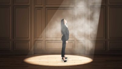 A businesswoman stands in a spotlight.