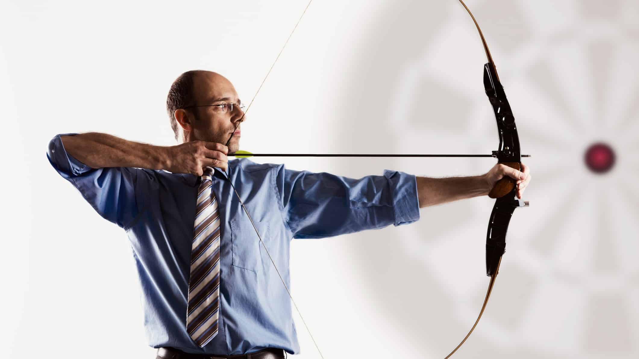 Business executive aiming bow and arrow at target.