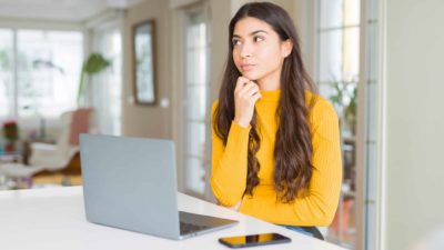 Young woman using computer laptop with hand on chin thinking about question, pensive expression.