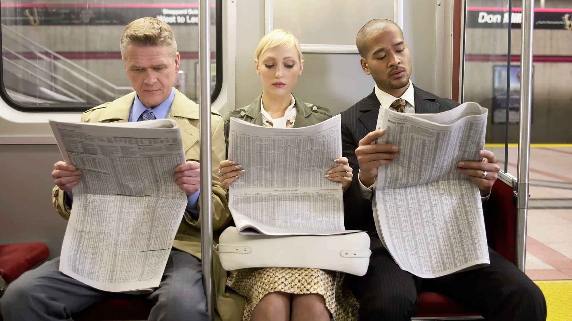 Two men and a woman sitting in a subway train side by side, reading newspapers.
