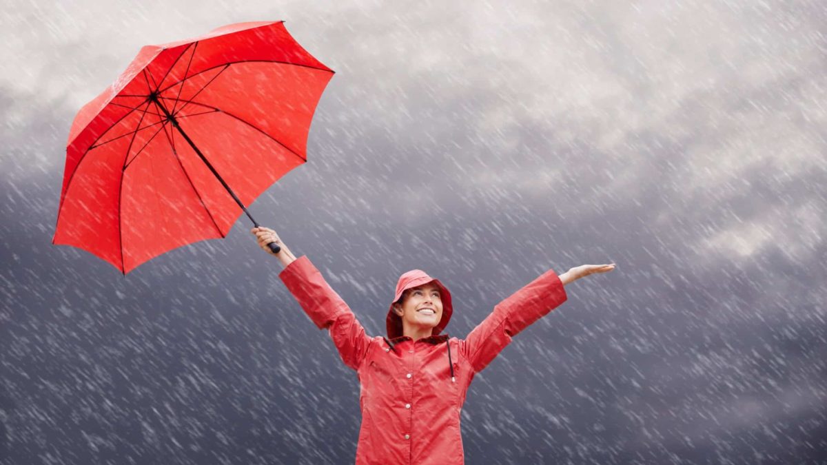 A young woman standing outside while holding her red umbrella in the rain.