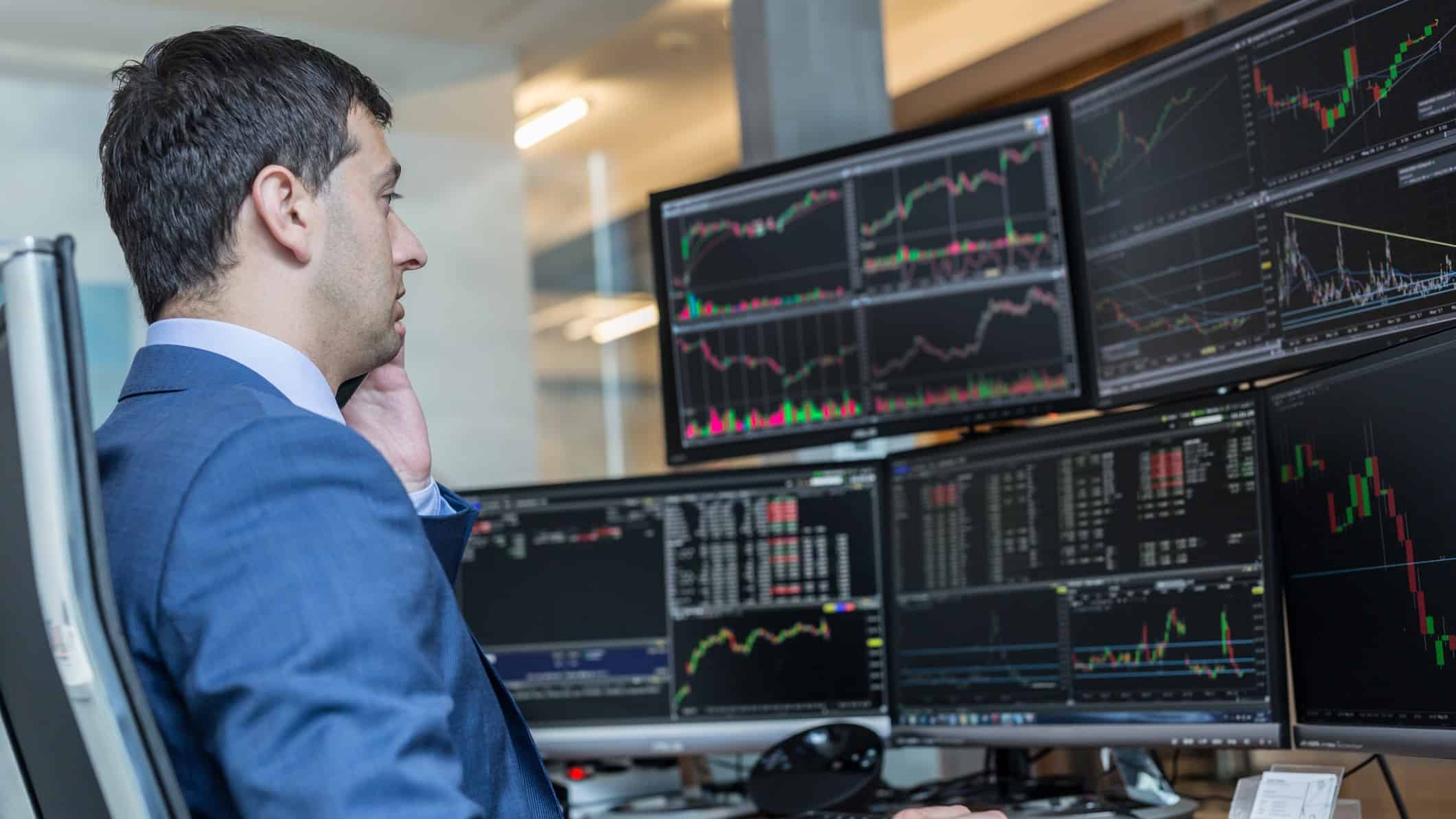 A share market analyst looks at various computer screens in front of him showing stock price movements