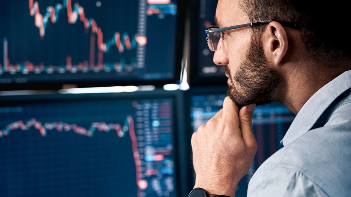 An ASX 200 market analyst holds his hand to his chin and looks closely at his computer screens watching share price movements