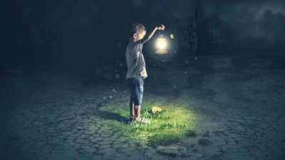 A boy holds up a lamp shining dimly in the dark.