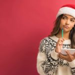 A woman wearing a red Santa hat thinks about what to write on her list.