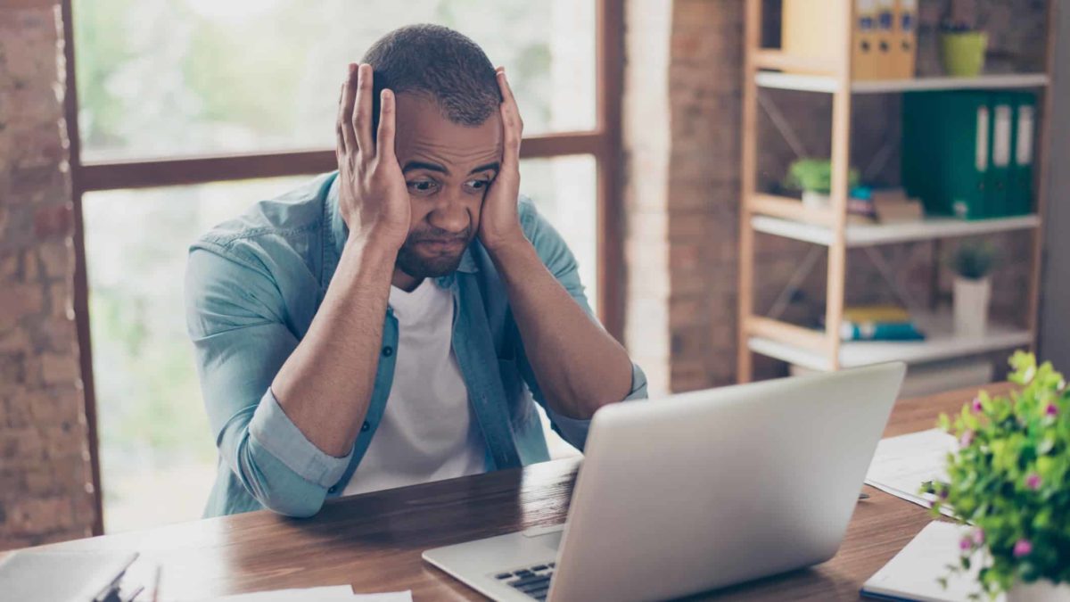 A man holds his head in his hands after seeing bad news on his laptop screen.