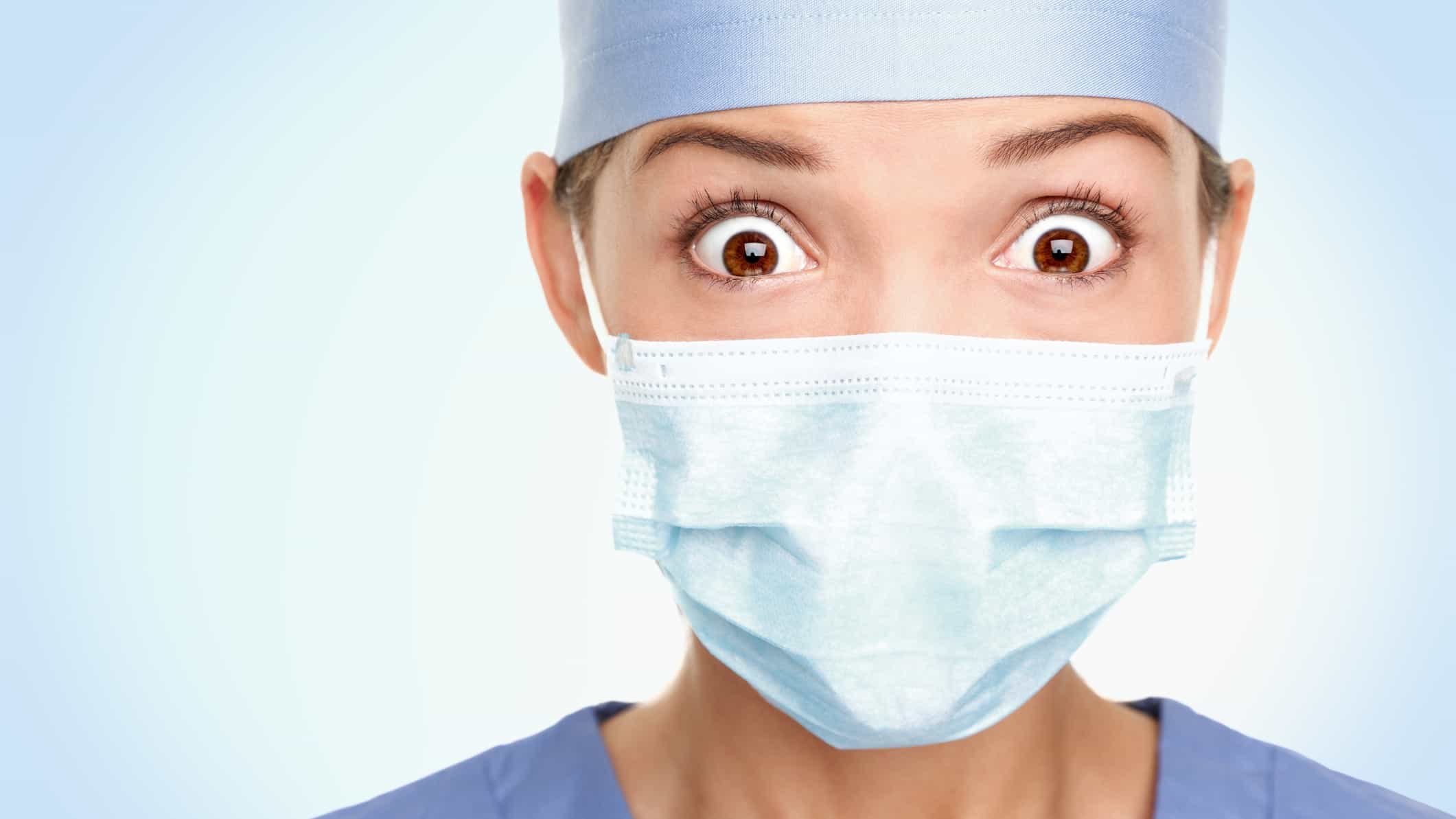 A female health professional has a wide-eyed shocked expression on her face, even behind the face mask.