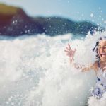 A young girl in a surging ocean wave on a sunny day.