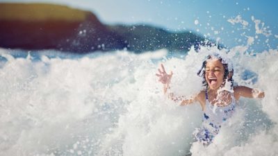 A young girls frolicks in a surging ocean wave on a sunny day.