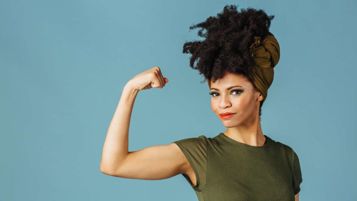 A woman wearing green flexes her bicep.